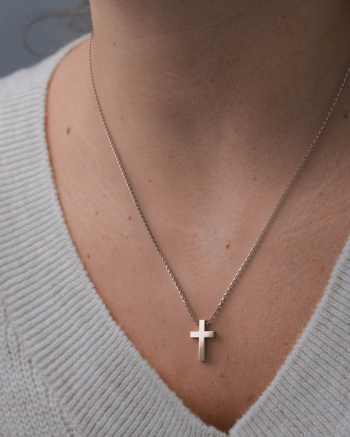 Silver cross necklace worn by a woman in a white V-neck