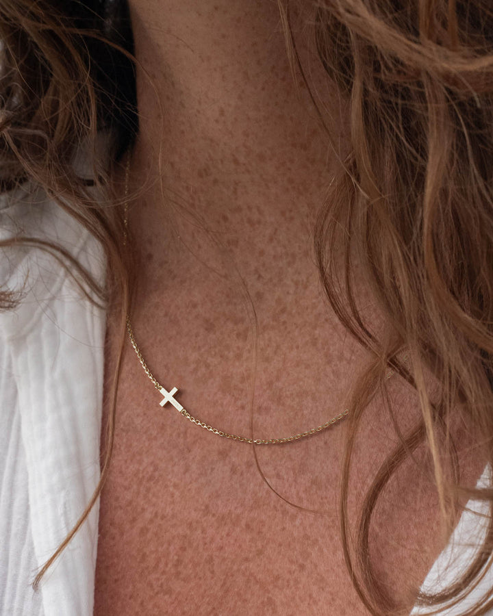 Gold side cross necklace worn by a woman