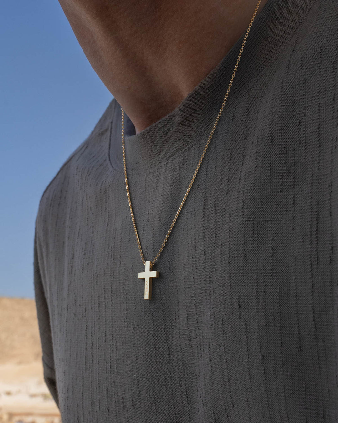 Gold cross necklace worn by a man in a grey t-shirt