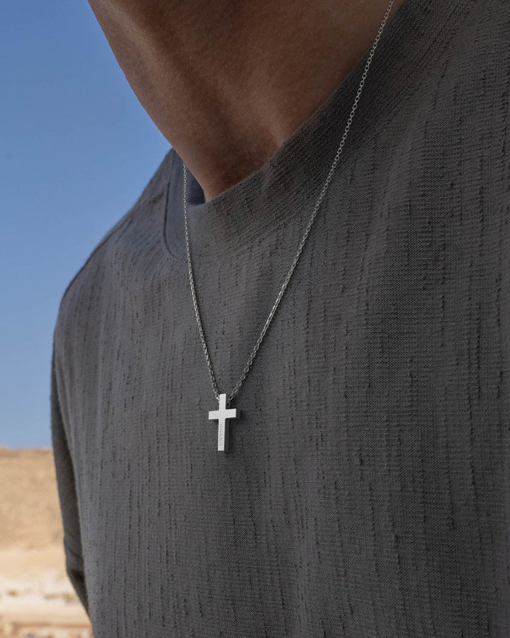 Silver cross necklace worn by a man in a grey t-shirt
