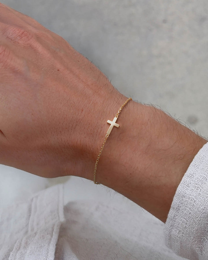 Gold side cross bracelet worn on a man's wrist