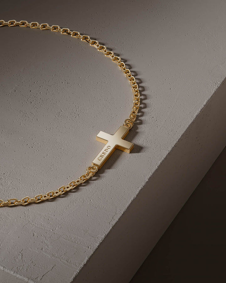 Side cross bracelet in gold, close-up of the cross on a stone block